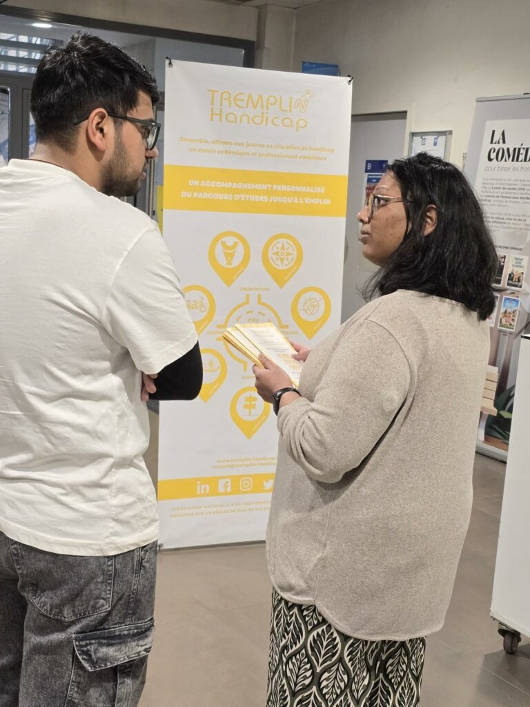 Une chargée d'accompagnement, parlant avec un jeune debout face à un kakémono de TREMPLIN Handicap